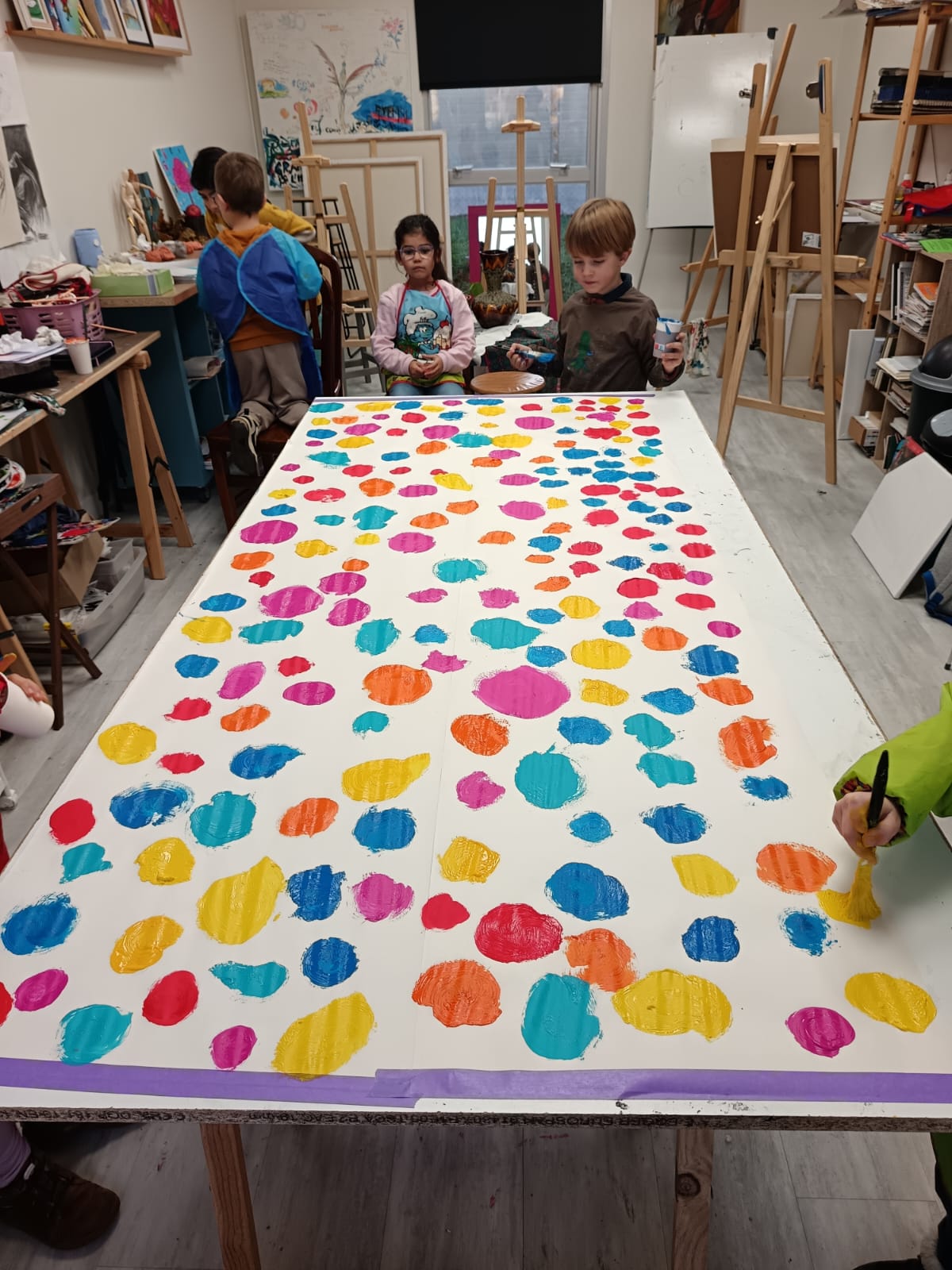 Grande toile collective couverte de pastilles de peinture réalisée par les enfants